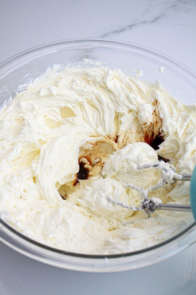 cheesecake batter being mixed in a large glass bowl.