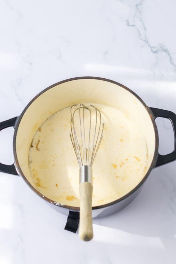 alfredo sauce being made in a dutch oven on the stove.