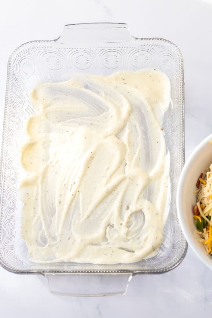 ranch alfredo sauce being spread on the bottom of a casserole dish.