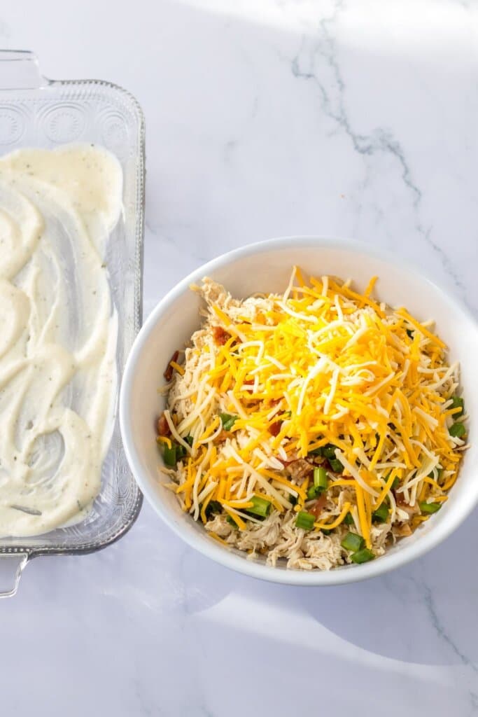 cooked chicken, shredded cheese, cooked bacon, and green onions being mixed together in a small bowl.
