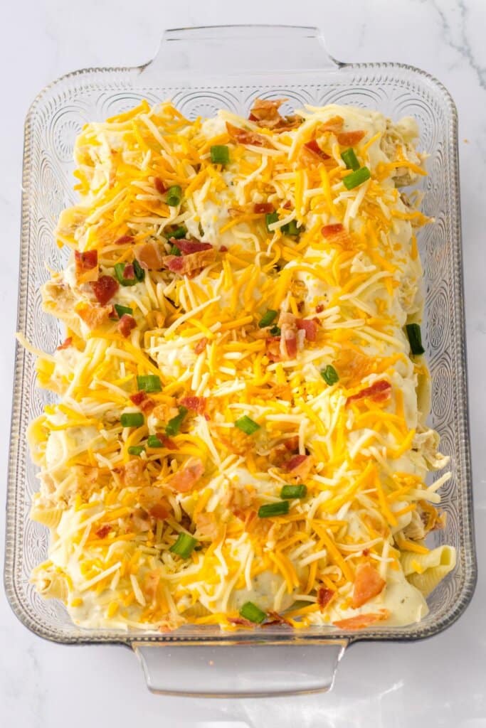 cheese, bacon, and green onions being sprinkled on top of the casserole.