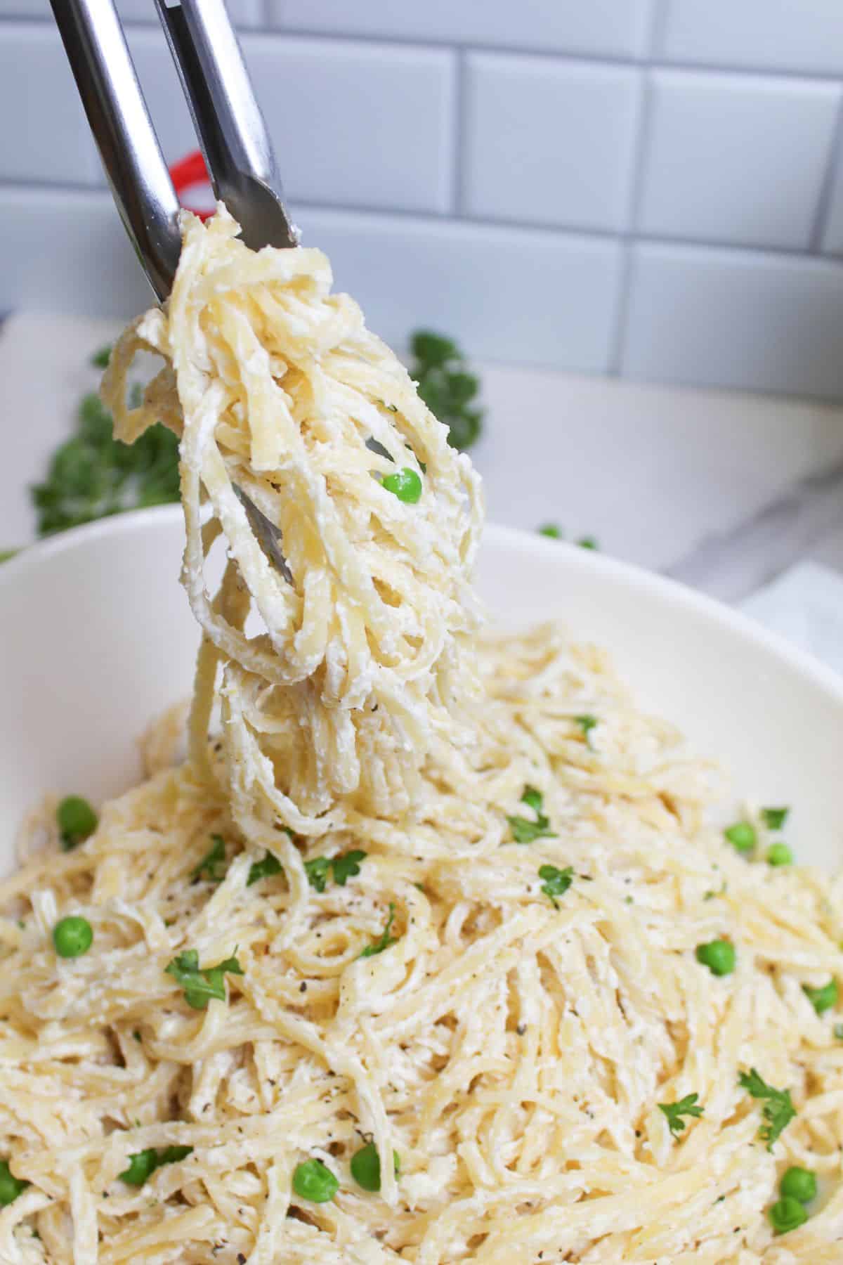 cream cheese pasta being removed from a bowl with tongs.