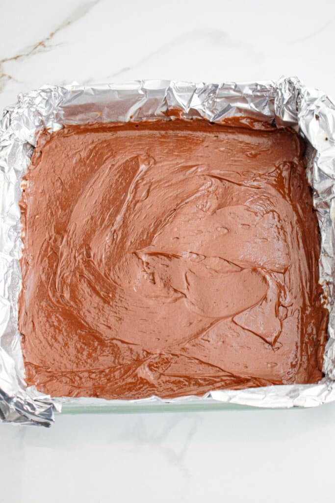 chocolate cheesecake filling being spread into a foil lined baking dish.