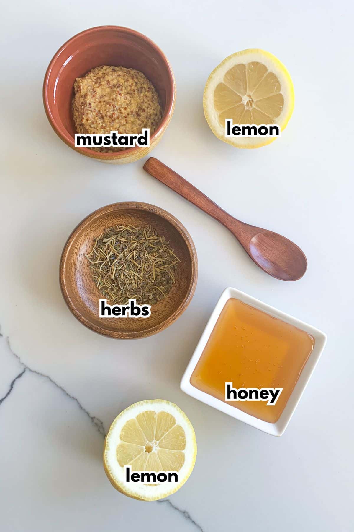 bowls of mustard, herbs, lemon, and honey on a counter.