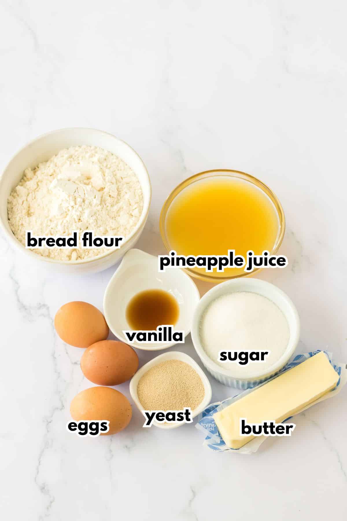 bowls of bread flour, pineapple juice, eggs, vanilla, yeast, sugar, and butter on a counter.