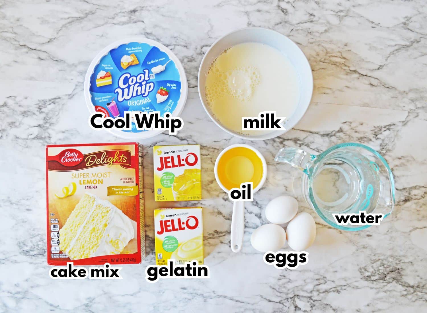 bowls of cool whip, milk, cake mix, gelatin, oil, eggs, water on a counter.