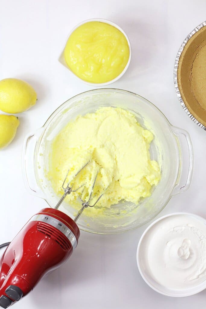cream cheese and lemon pie filling being mixed in a glass mixing bowl.