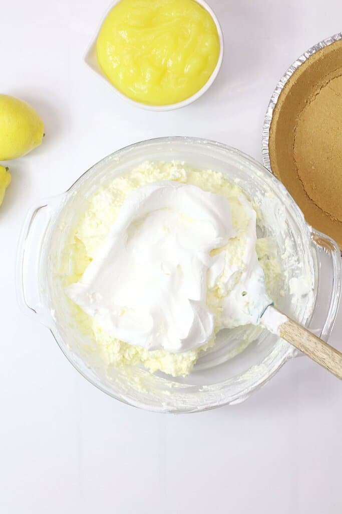 cool whip being added to pie filling in a glass bowl.