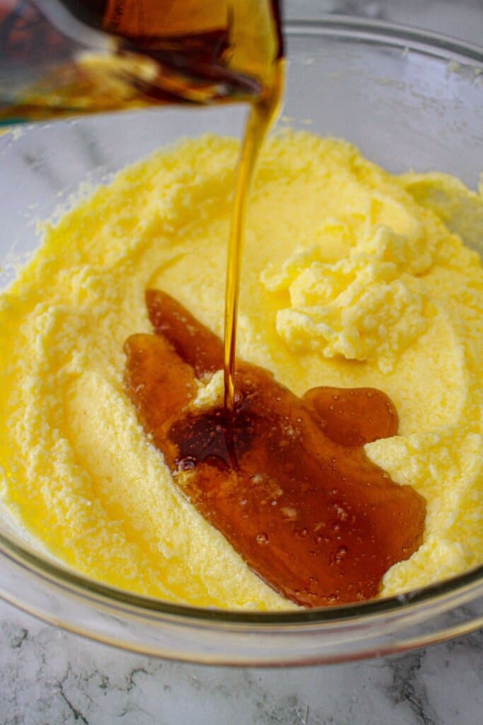 maple syrup being poured into creamed butter and sugar.