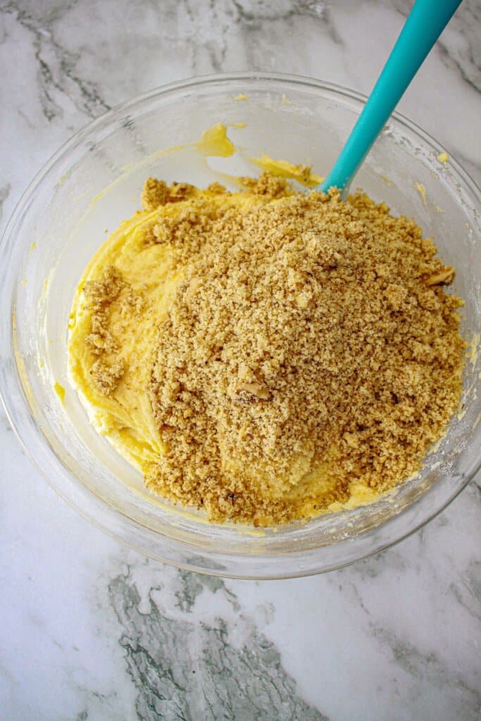 crushed walnuts being added to cake batter in a glass mixing bowl.