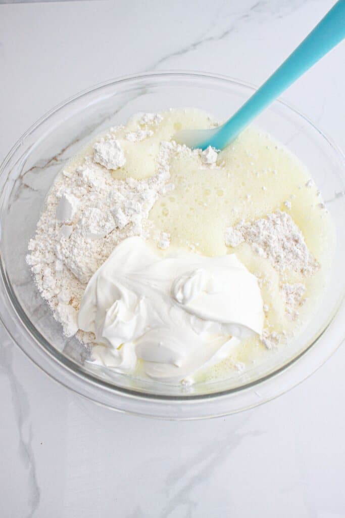bisquick, sour cream, and mountain dew being mixed in a glass mixing bowl.
