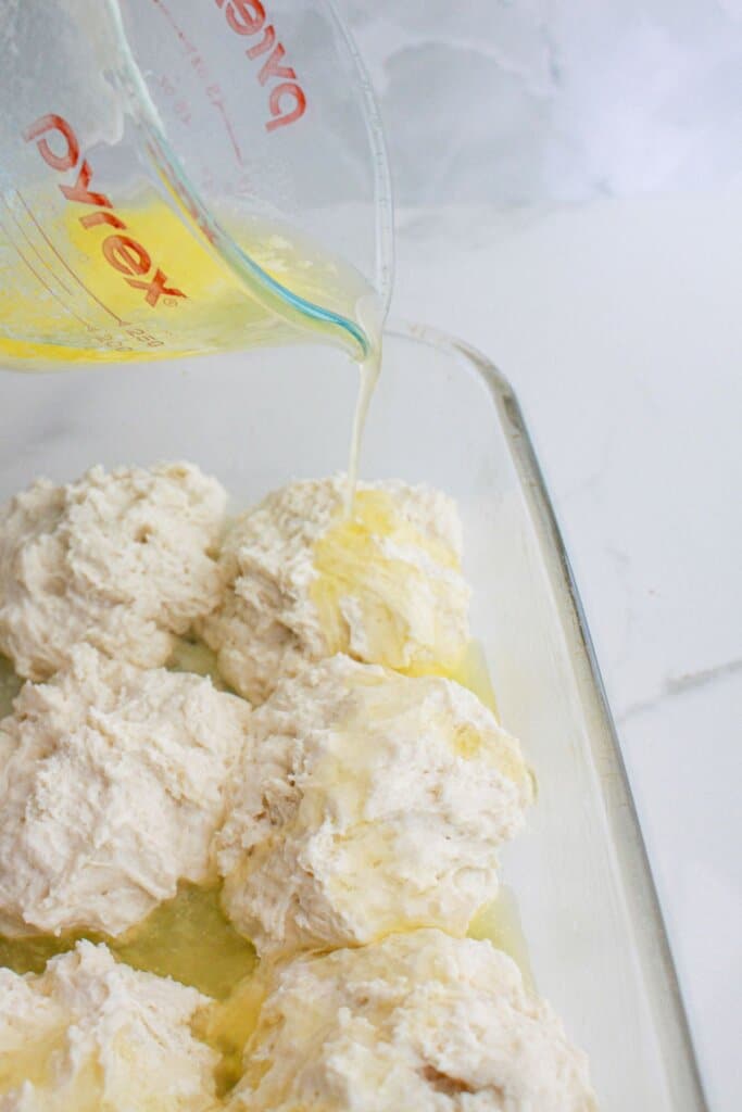 butter being poured over biscuit dough in a glass baking dish.
