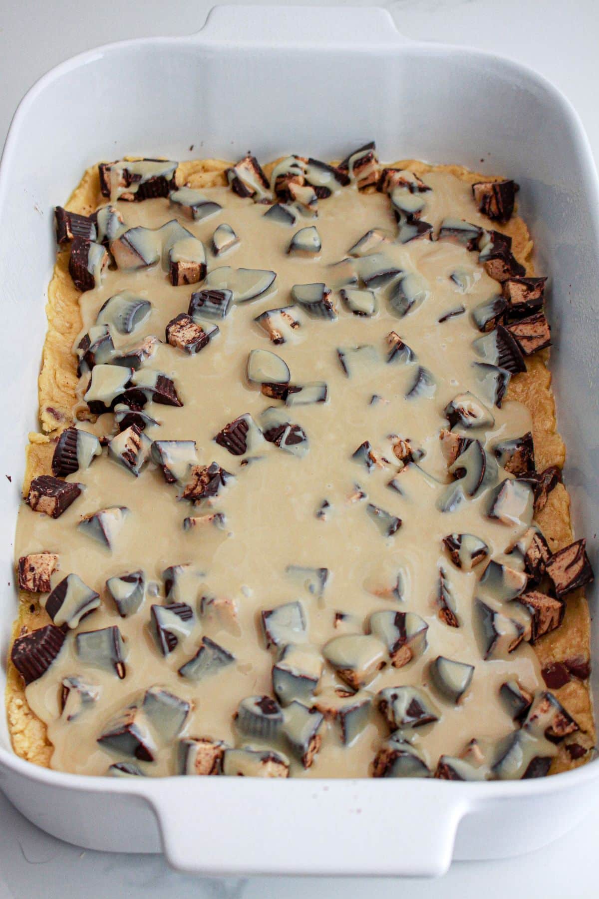 peanut butter cups and peanut butter filling being poured on top of cookie dough.