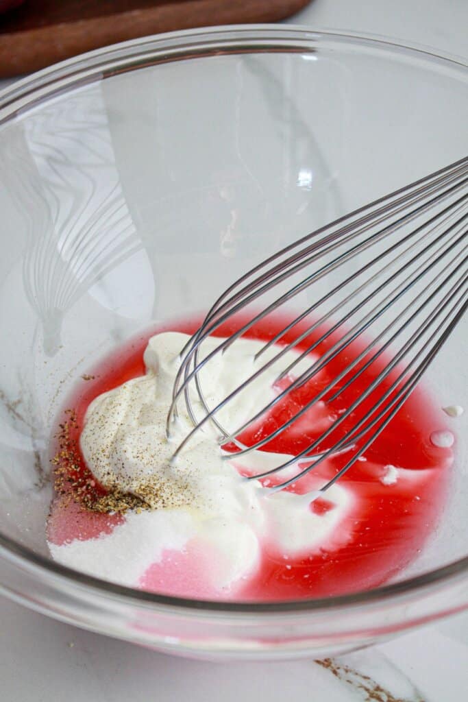 dressing ingredients being mixed in a large glass mixing bowl with a whisk.