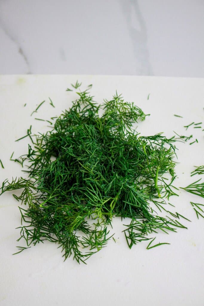 fresh dill being chopped on a cutting board.