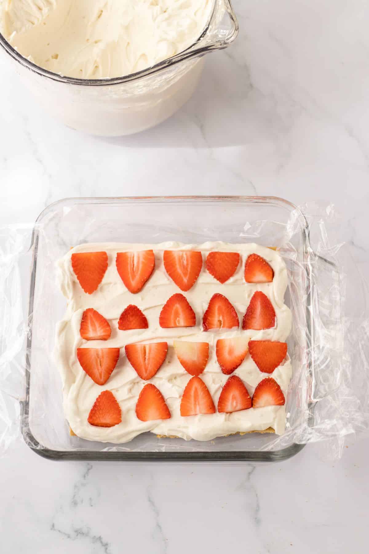 strawberries being layered on top of cream cheese layer.