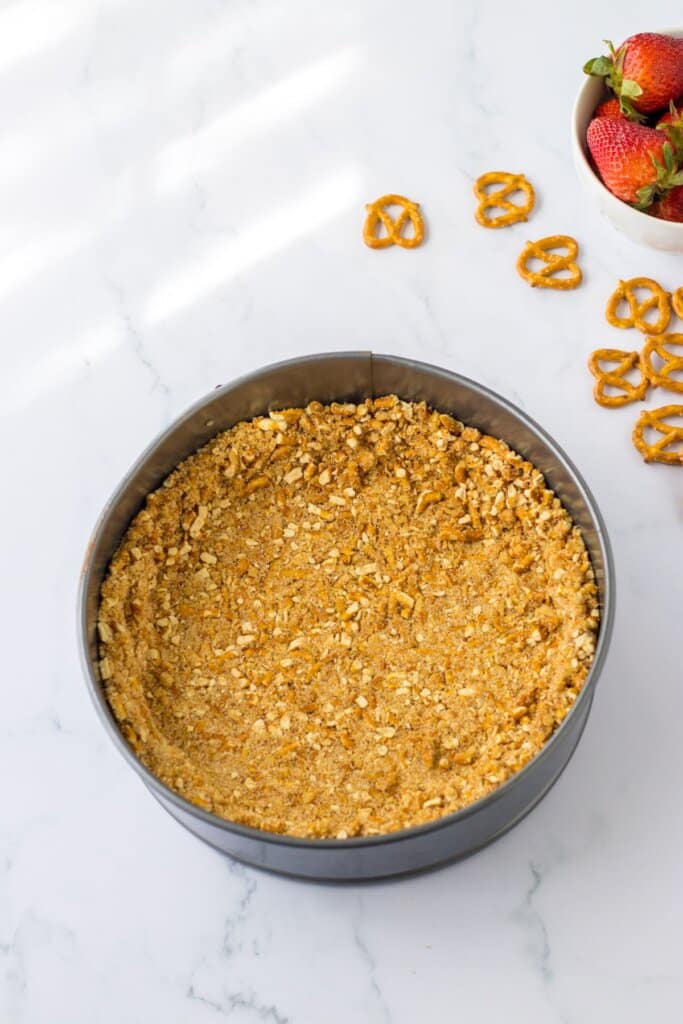 pretzel crust being pressed into a spring form pan.
