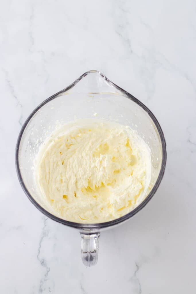 whipped cream being made in a glass mixing bowl.