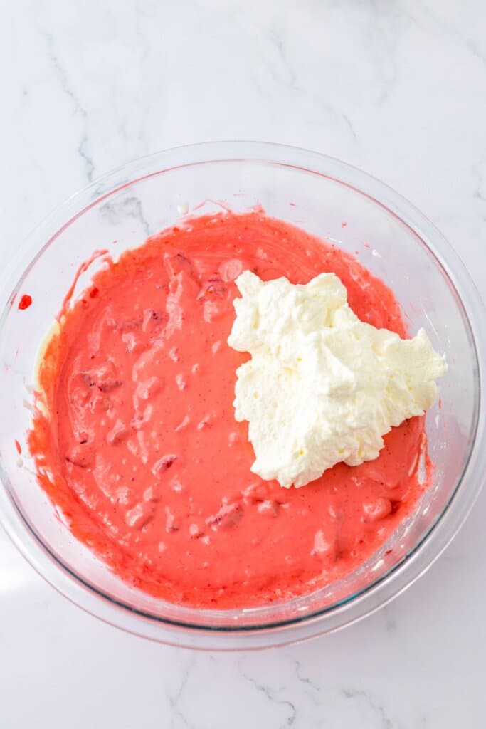 whipped cream being added to strawberry gelatin mixture.