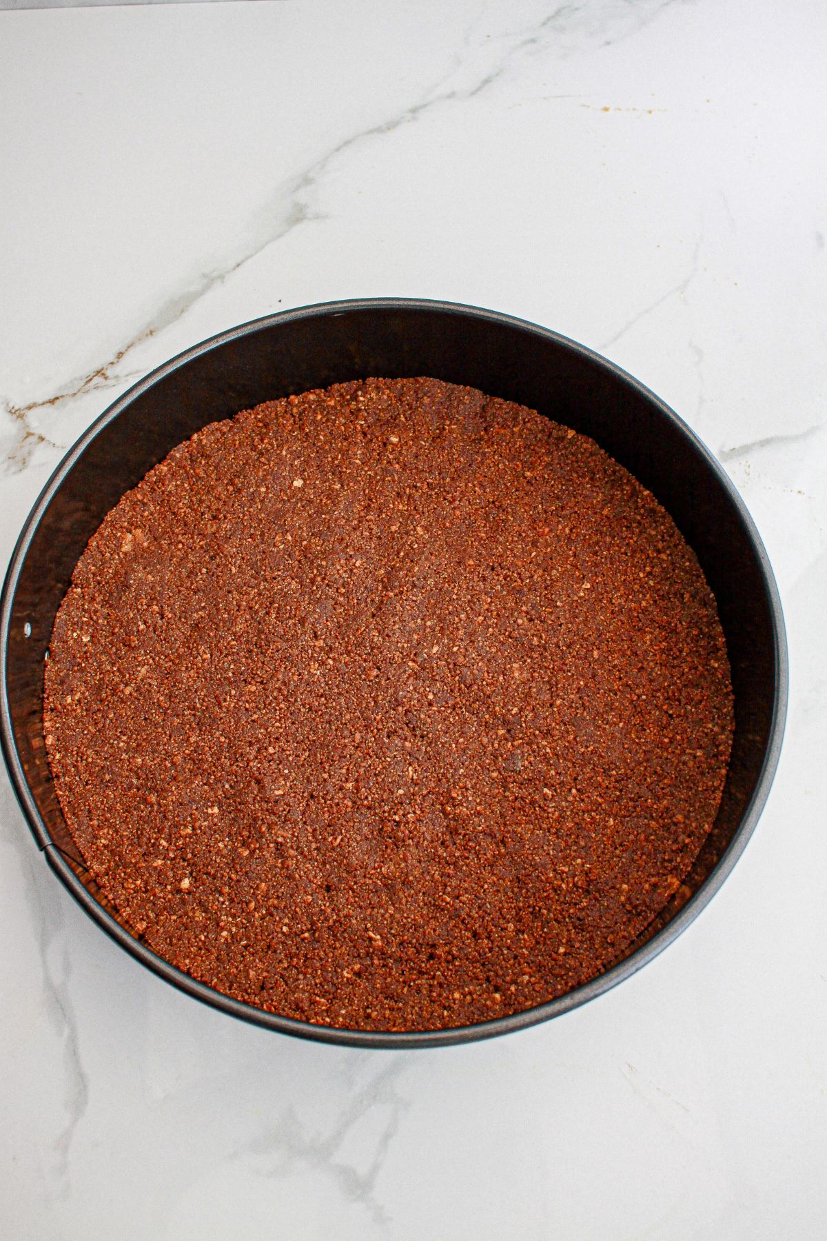 graham cracker crust being pressed into a springform pan.