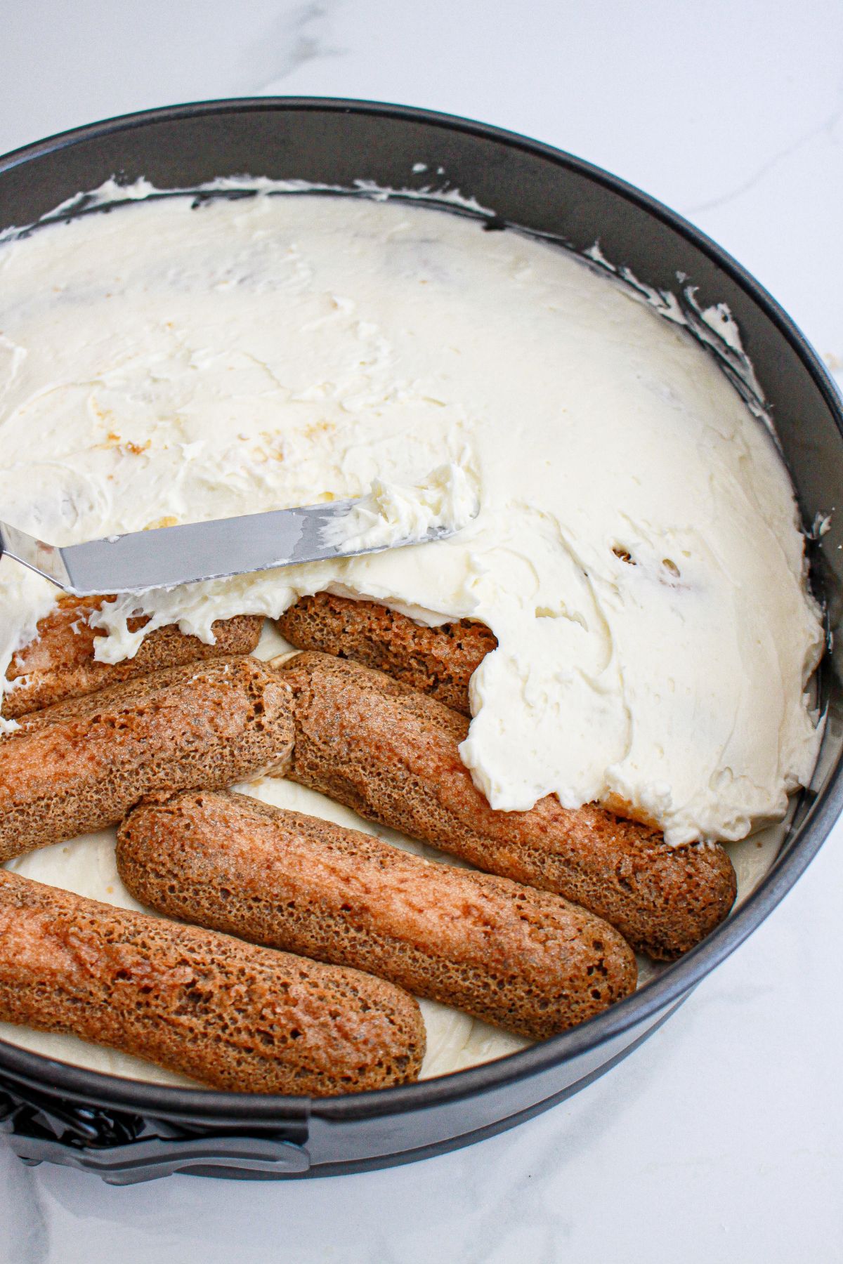 cheesecake layer being spread on top of lady fingers in a springform pan.