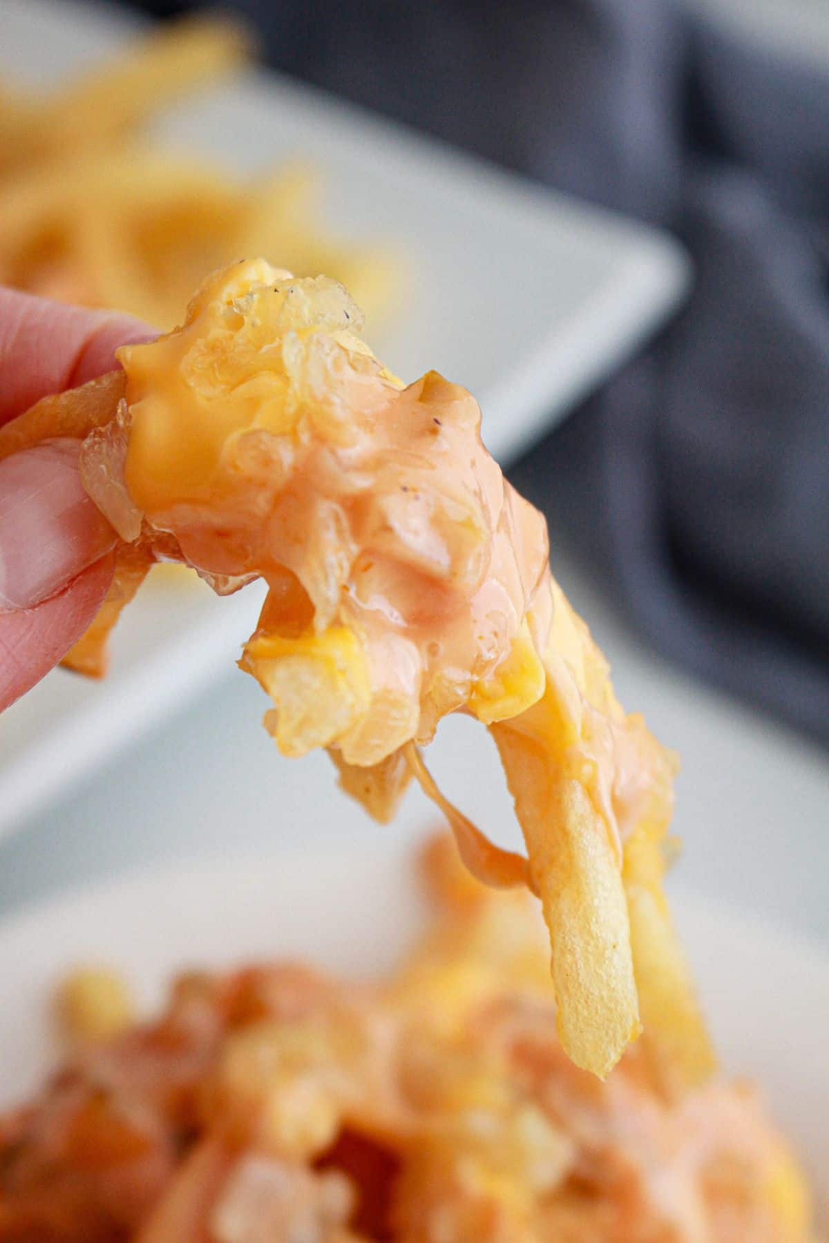 bite of animal style fries held in a woman's fingers in the air.