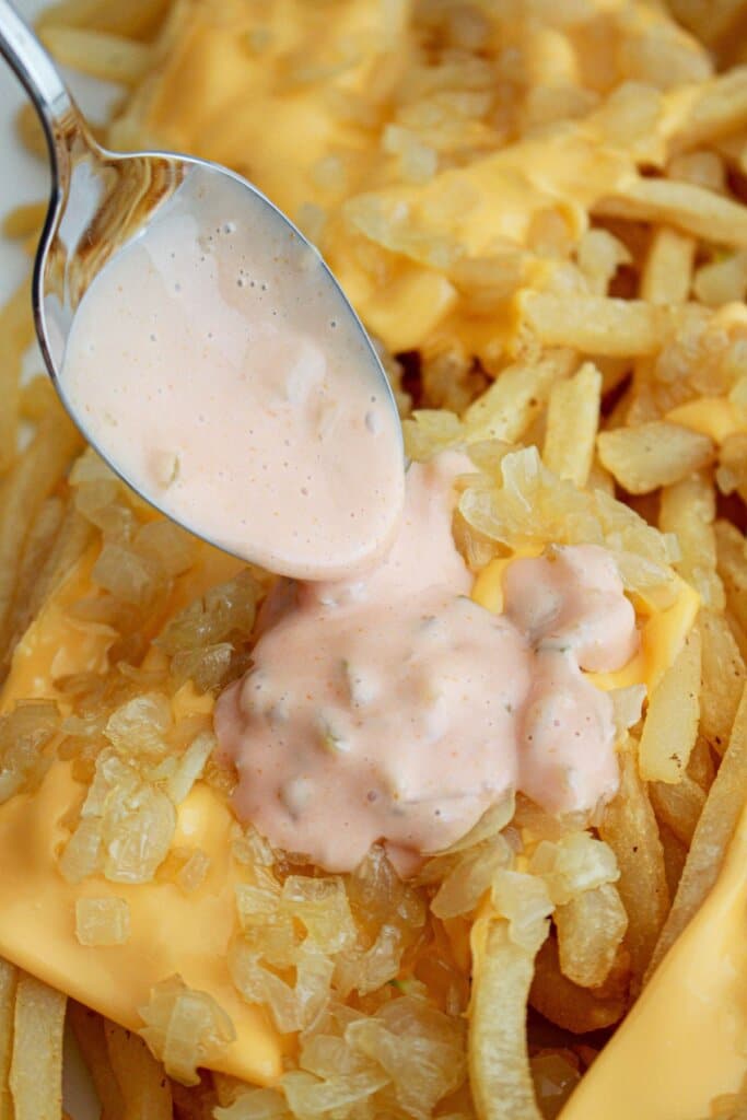 sauce being poured over french fries on a platter.