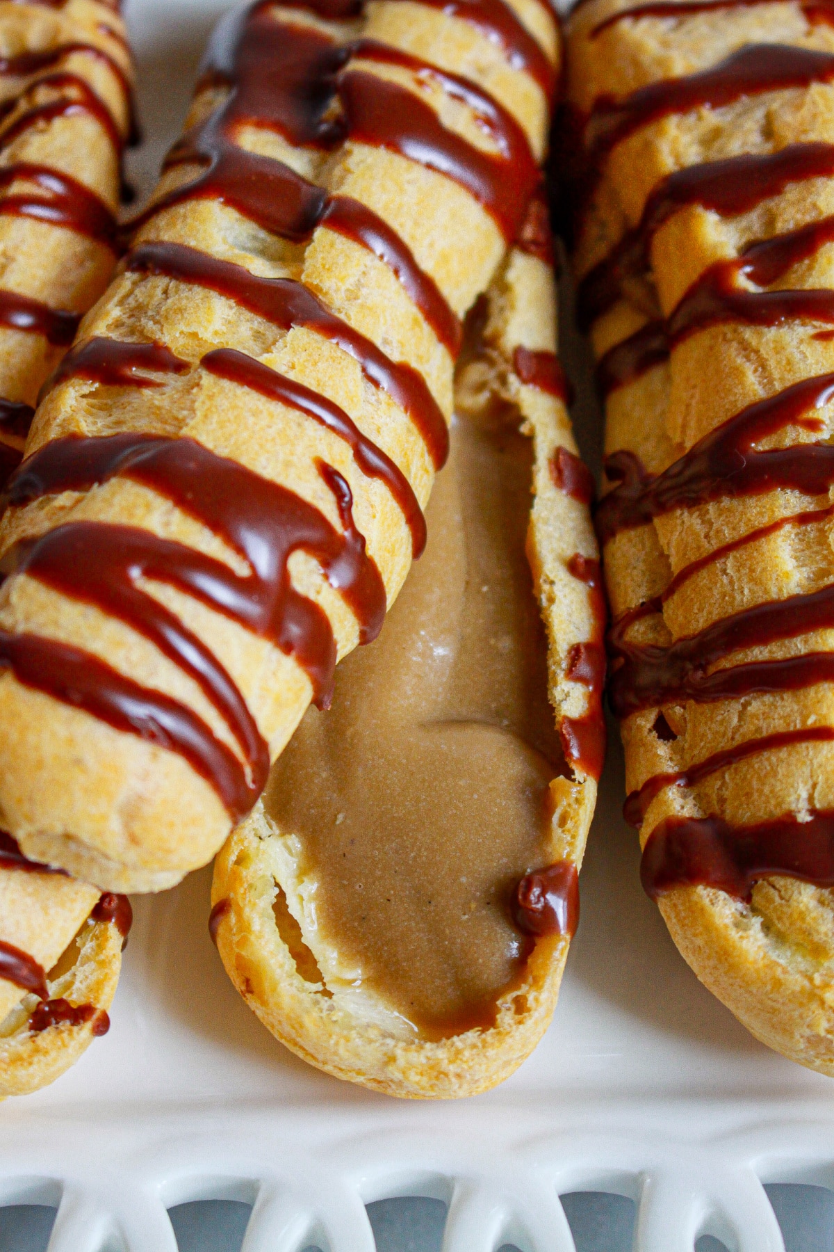 three cappuccino eclairs on a plate with one cut open.