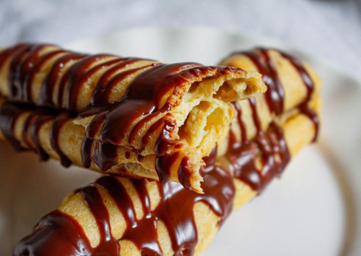 two cappuccino eclairs on a plate with one broken in half.