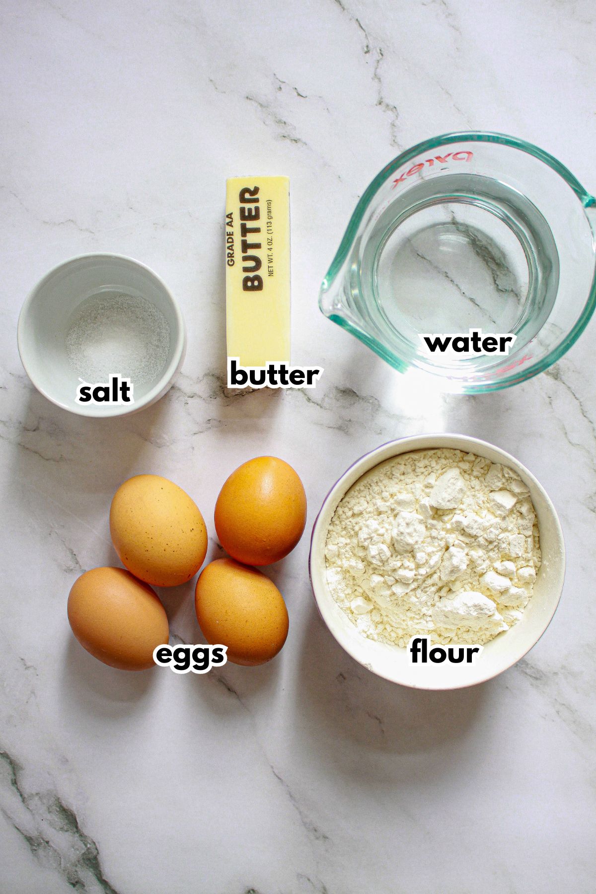bowls of salt, butter, water, eggs, and flour on a counter.