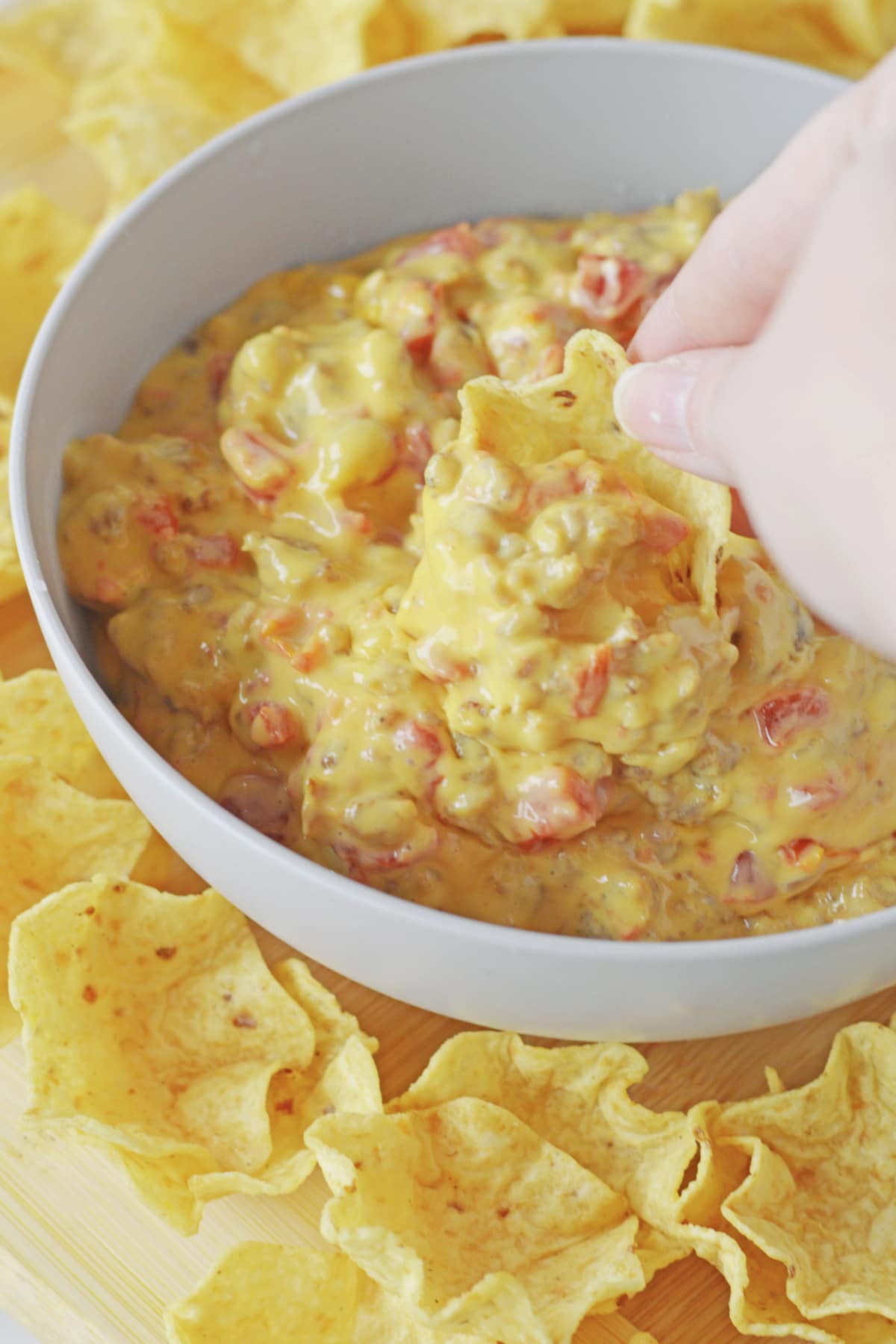 tortilla chip being dipped into a bowl of cheese dip.