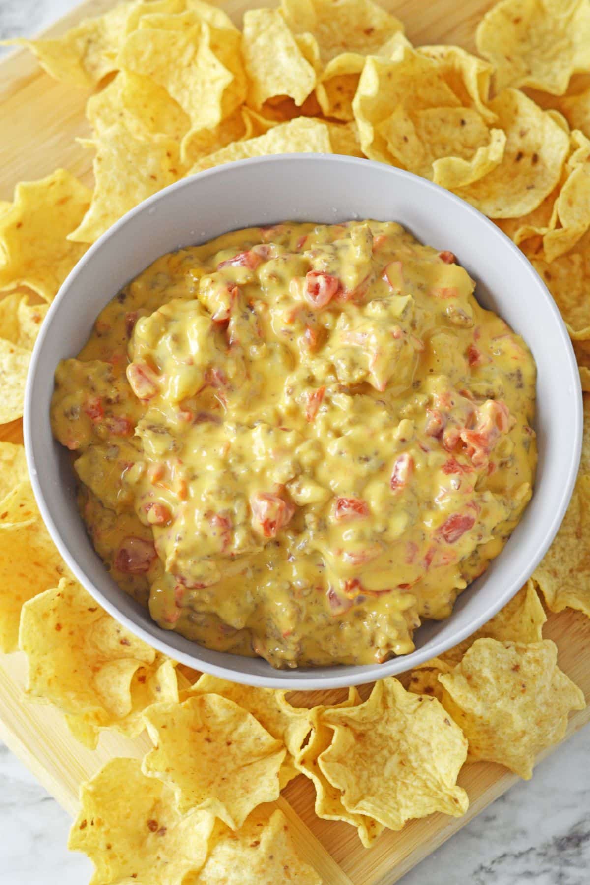 bowl full of cheese and rotel dip surrounded by tortilla chips.