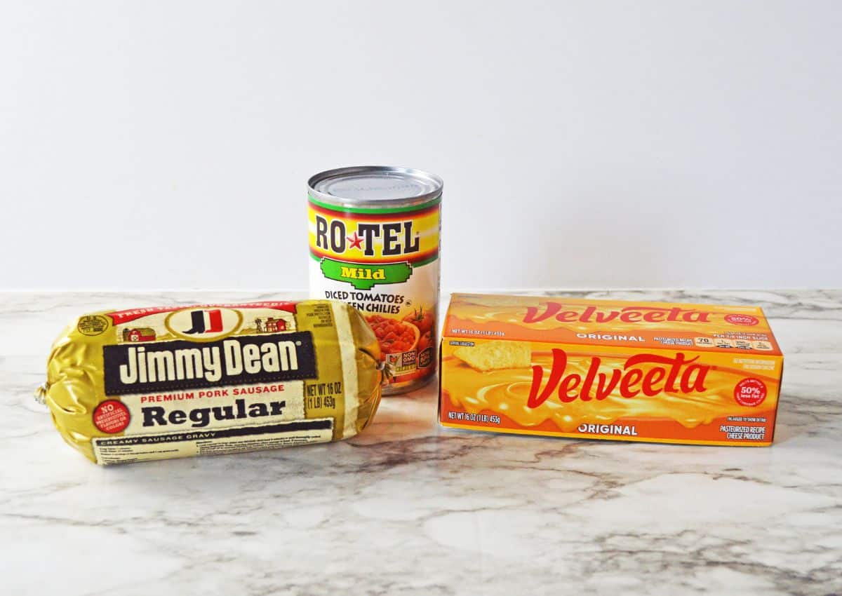 a can of rotel, roll of sausage, and box of velveeta on a counter.