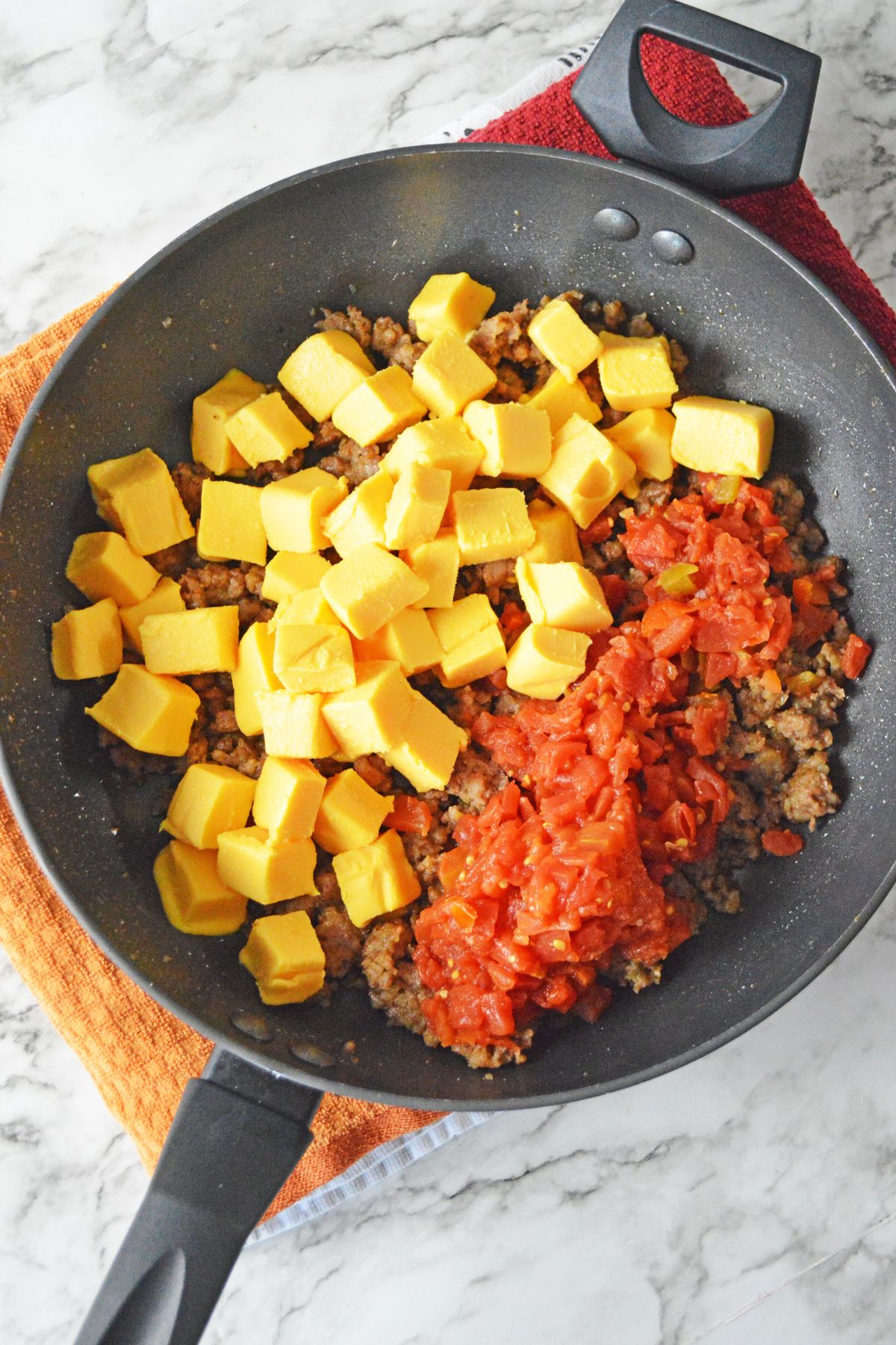 cheese, tomatoes, and cooked sausage being heated in a large skillet.