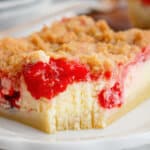 slice of cherry pie cheesecake bar on a plate with a bite missing.