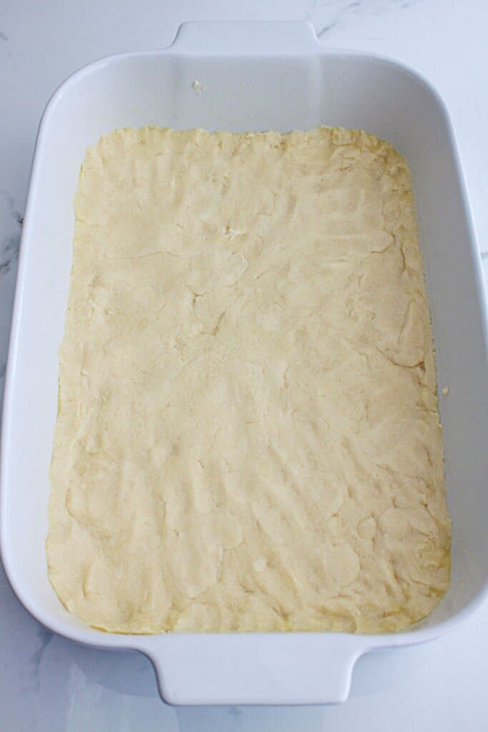 shortbread crust being pressed into a baking dish.