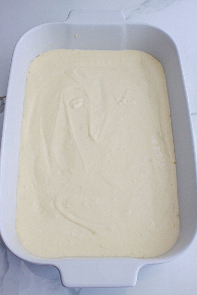 cheesecake layer being spread in a baking dish.