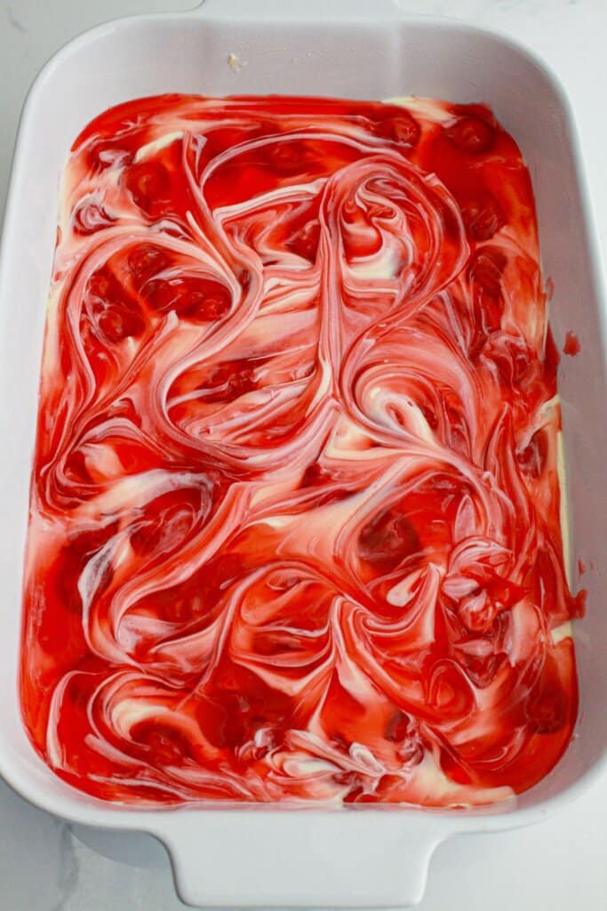 cherry pie filling being swirled on top of bars