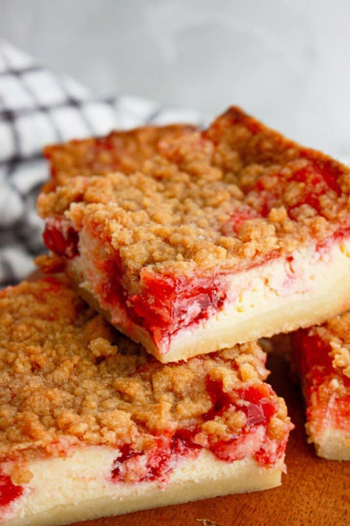 three cherry pie cheesecake bars stacked on a plate.
