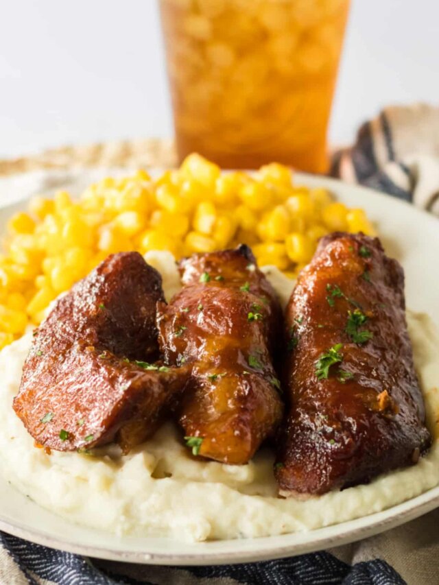 three honey bbq ribs on a plate with mashed potatoes and corn.