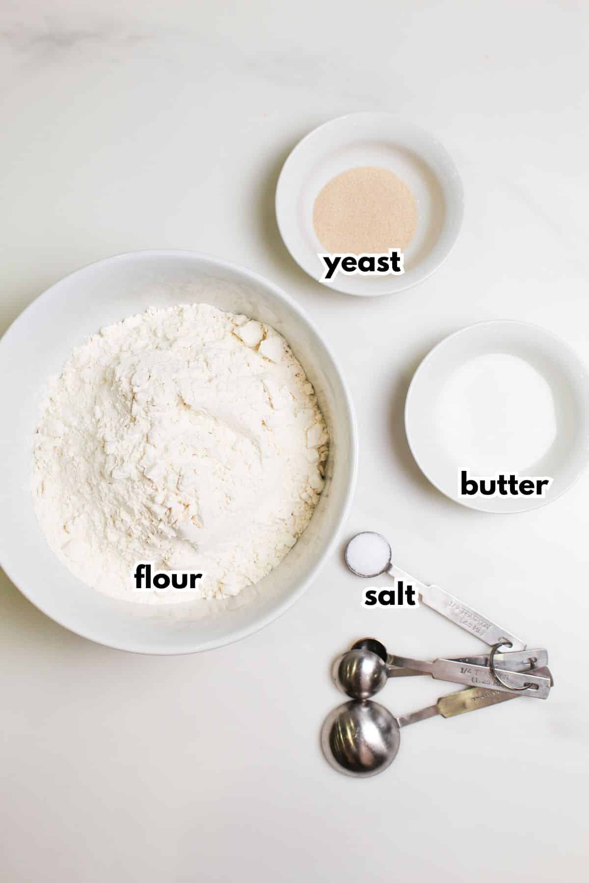 bowls of flour, yeast, butter, and salt on a counter.