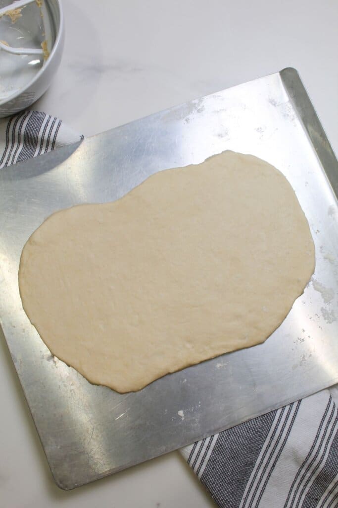 dough being rolled out on a baking dish.