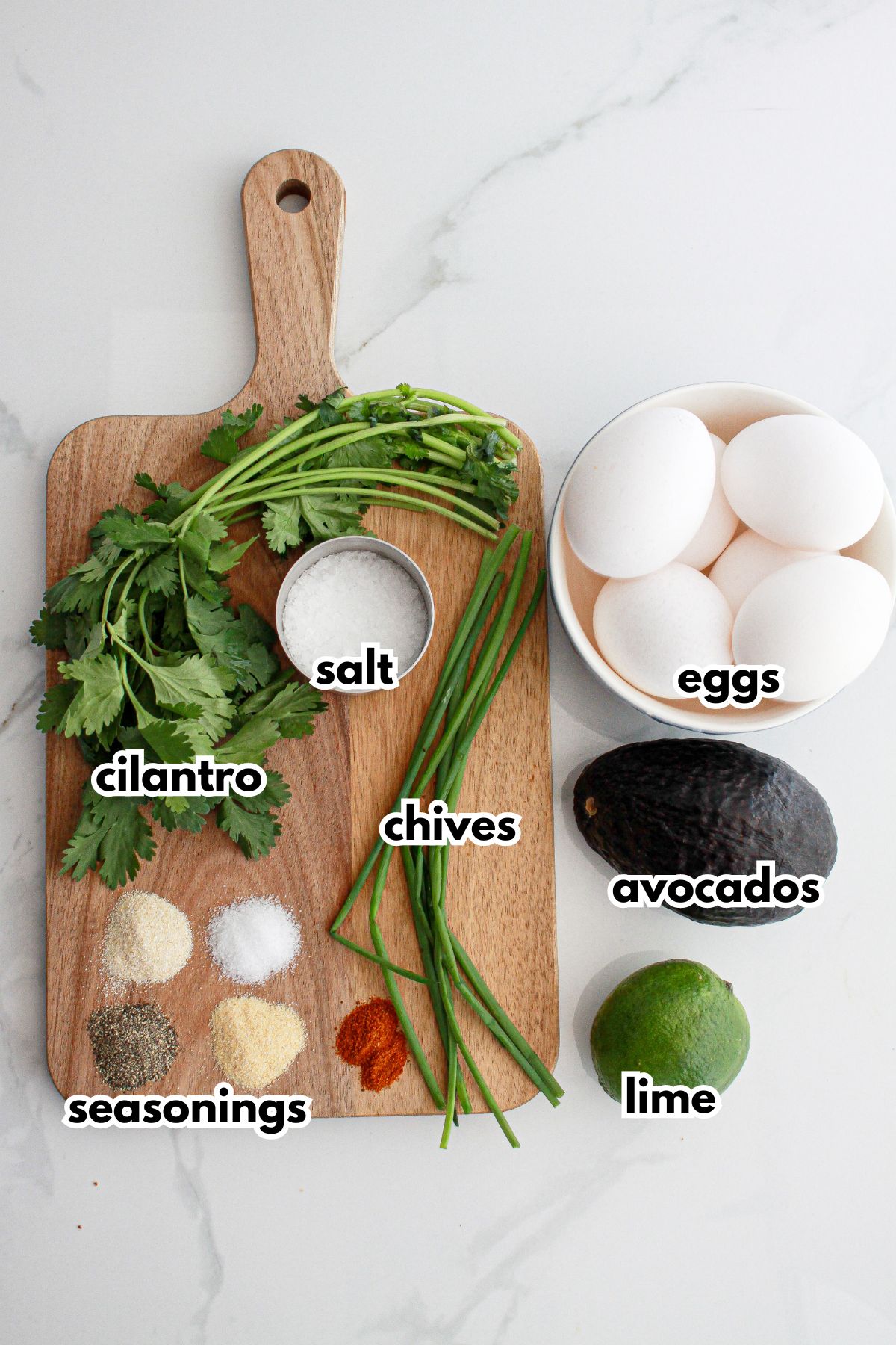 cilantro, salt, chives, seasonings, eggs, avocado and lime on a counter.