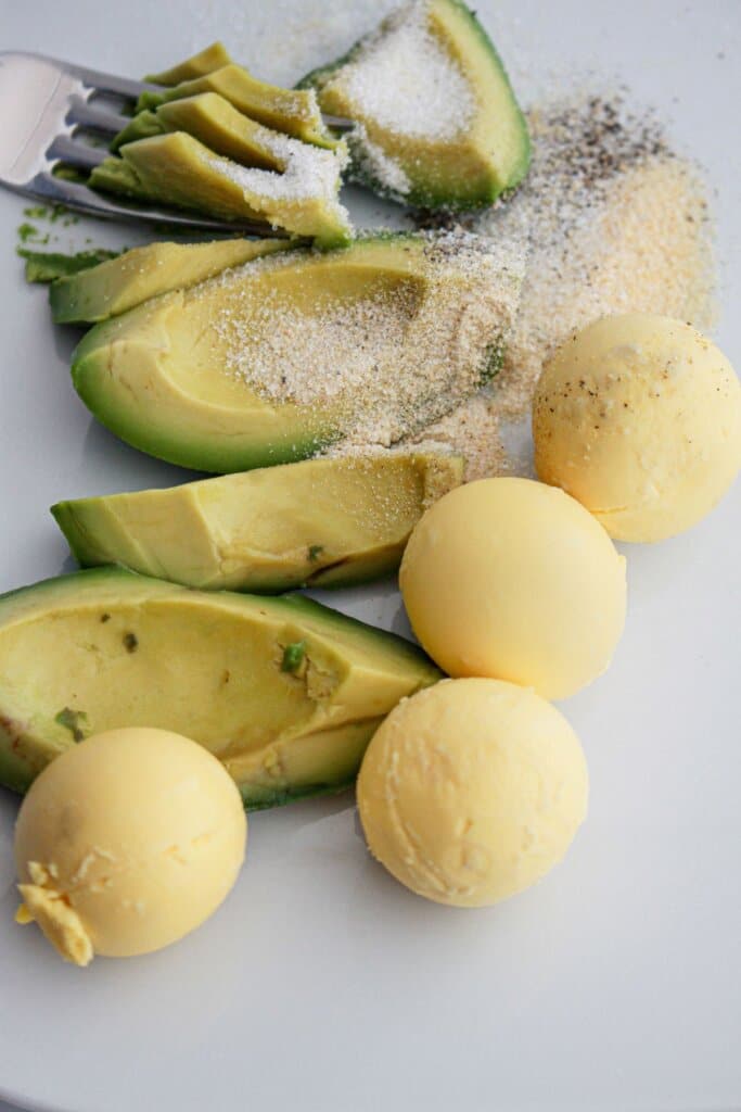 avocadoes, egg yolks, and seasonings being mashed together in a bowl.