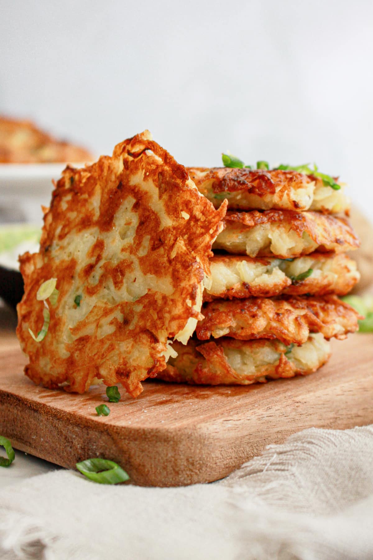 five hash brown pancakes stacked on a wooden cutting board.