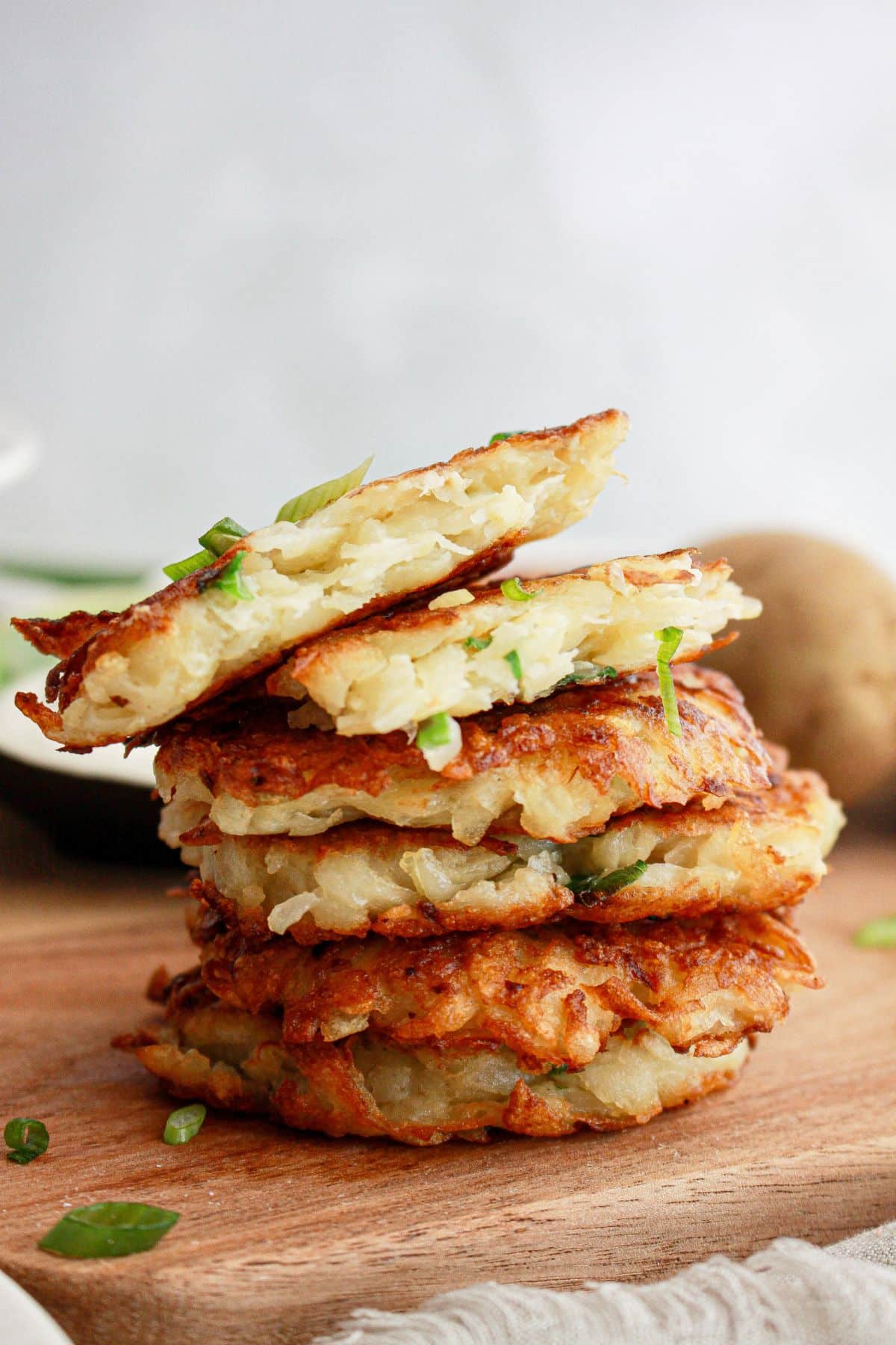 five hash brown pancakes stacked on top of each other on a cutting board with the top one broken in half.