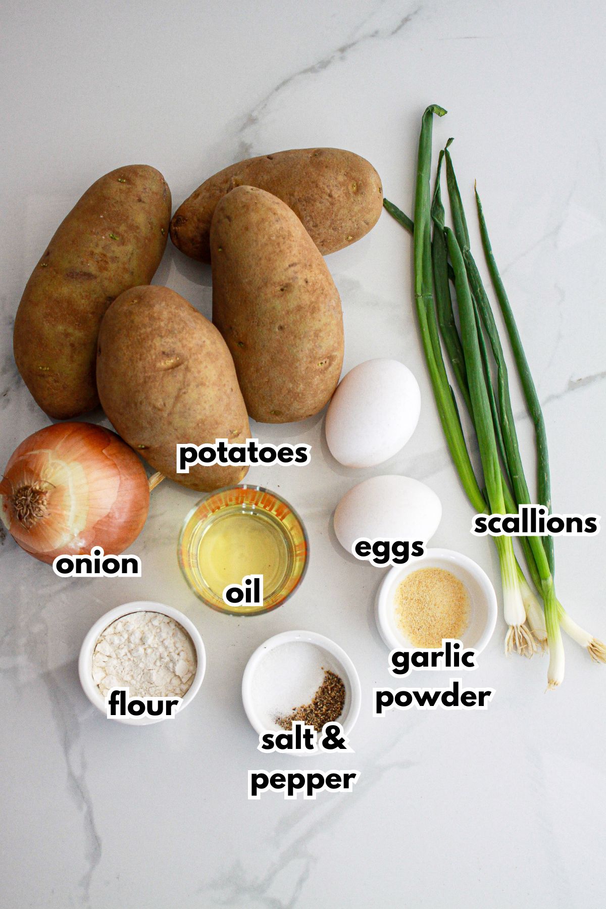potatoes, onion, eggs, flour, oil, salt, pepper, garlic powder, and scallions on a counter.