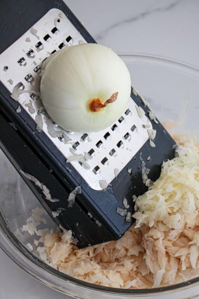 onion being shredded on a box grater into a mixing bowl.