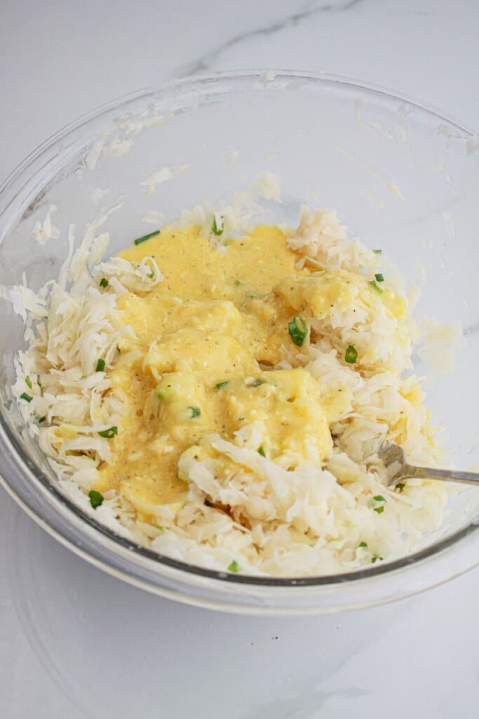 egg and flour mixture being mixed with shredded potatoes
