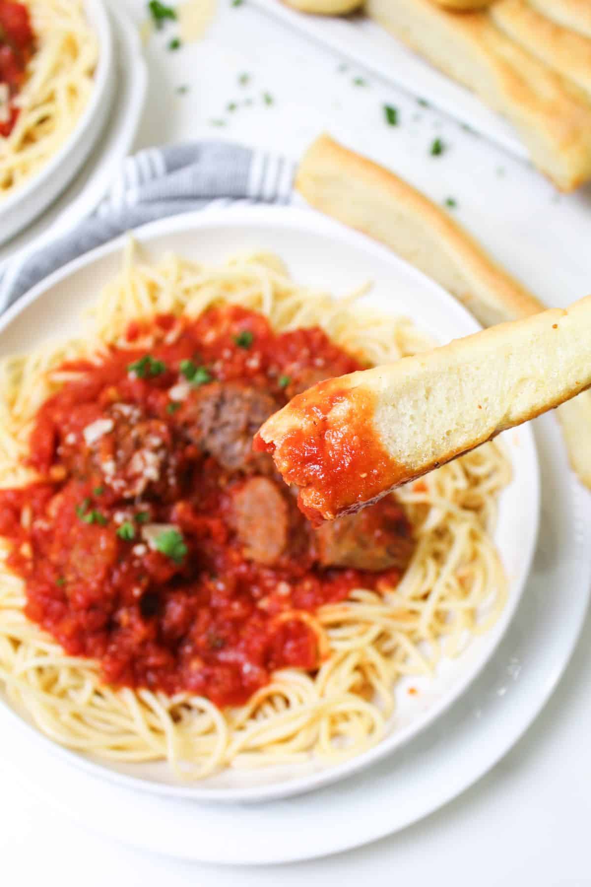 garlic breadstick dipped in homemade pasta sauce held in the air.
